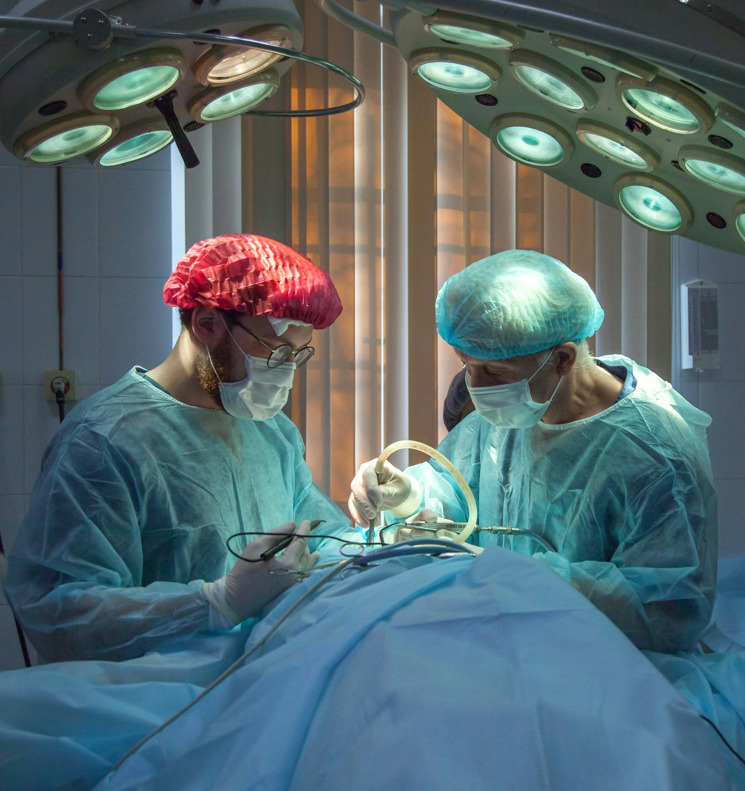 Zwei Chirurgen in OP-Kleidung bei einer Operation unter OP-Leuchten