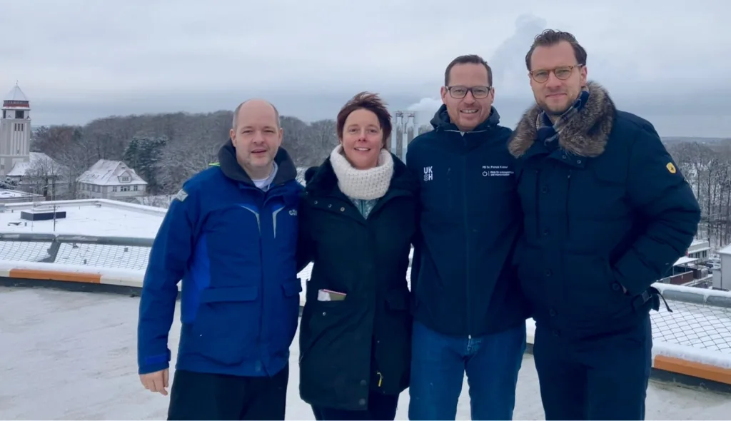 Vier Personen in Winterjacken auf einer verschneiten Dachterrasse