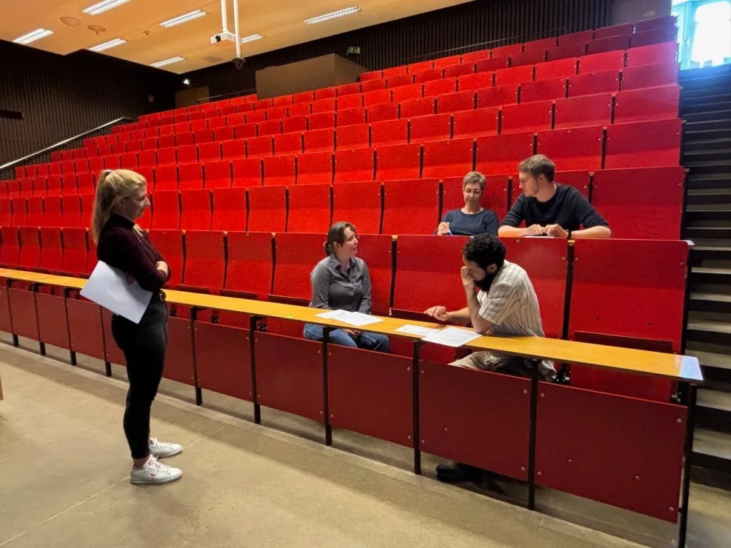 Kleingruppe diskutiert in einem Hörsaal mit roten Sitzen