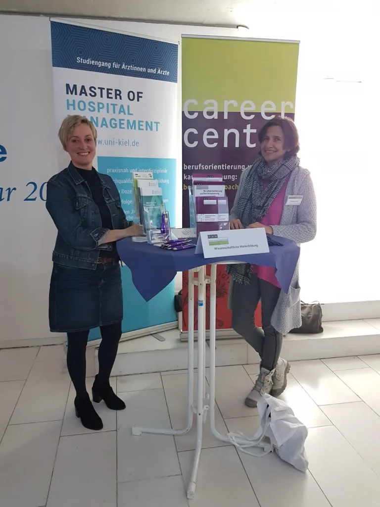 Zwei Frauen an einem Infostand mit Roll-up des Master of Hospital Management