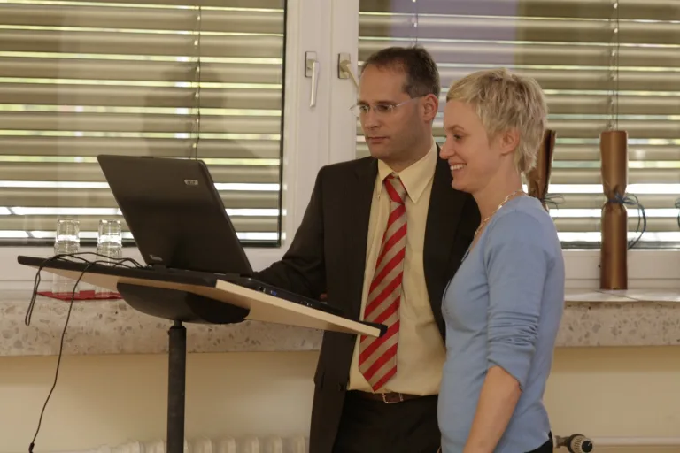 Ein Mann und eine Frau stehen lächelnd gemeinsam an einem Rednerpult mit Laptop