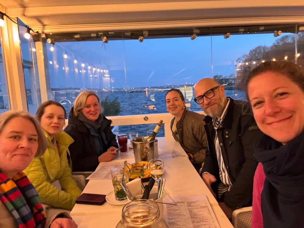 Gruppe lächelt in einem Restaurant mit Blick auf die Kieler Förde in der Abenddämmerung